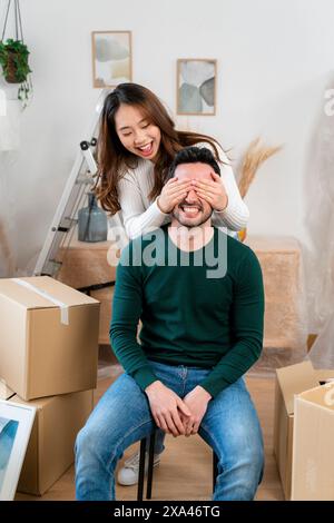 Frau überrascht Mann mit Händen über den Augen in einem Raum mit Umzugskästen. Stockfoto
