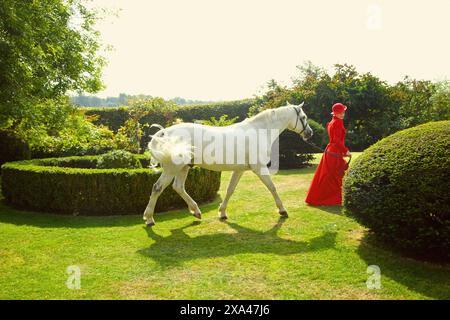 Frau in rot Reit Outfit zu Fuß im Garten mit Pferd Stockfoto