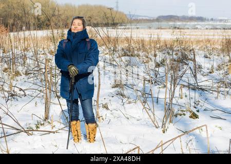 Frau, die auf dem schneebedeckten Feld steht und die Stange zum Wandern hält Stockfoto