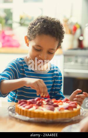 Junge, der Erdbeeren zum Kuchen hinzufügt Stockfoto