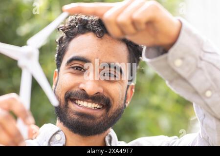 Ein lächelnder Mann mit Bart, der eine Miniatur-Windenergieanlage hält Stockfoto
