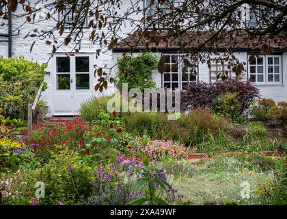 Altes ländliches weißes Dorfhaus mit weißen Wänden und farbenfrohem Landhausgarten. Stockfoto