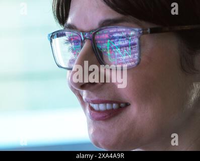 Eine Nahaufnahme einer lächelnden Frau, die eine Brille trägt, die eine bunte Grafik reflektiert. Das Bild konzentriert sich auf ihr Profil und zeigt ihre Brille und ihren fröhlichen Ausdruck. Stockfoto