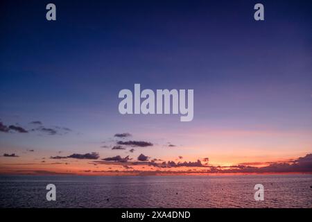 Eine ruhige Meereslandschaft bei Sonnenuntergang mit leuchtenden Orange- und Violetttönen, die den Himmel und sanfte Wellen auf der Wasseroberfläche bemalen. Stockfoto