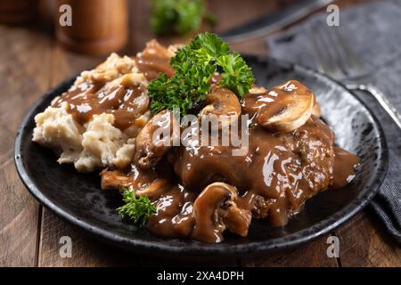 Salisbury-Steak mit Pilzsoße garniert mit Petersilie und Kartoffelpüree auf einem schwarzen Teller Stockfoto