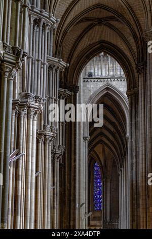 Das Bild zeigt das Innere einer gotischen Kathedrale mit hohen Bogendecken, Rippengewölben und verzierten Säulen, mit einem Buntglasfenster im Hintergrund. Stockfoto