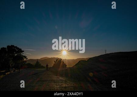 Das Bild zeigt einen atemberaubenden Sonnenuntergang mit Sonnenstrahlen, die durch den Himmel dringen und lange Schatten auf einem Pfad mit Silhouettenfiguren werfen. Stockfoto