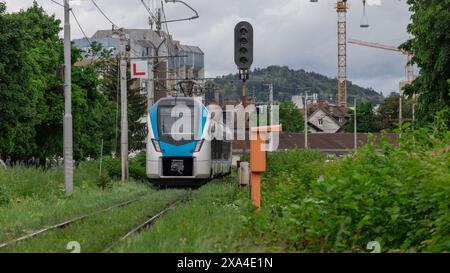 Der moderne Personenzug fährt auf schlechten und vernachlässigten Gleisen. Grüne Bahnstrecke, Blätter und Gras wachsen aus dem Kiesbett. Nicht Stabil Stockfoto