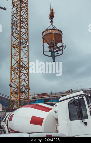 Betonierung beim Betonieren von Beton-Böden im Gebäude. Behälter für Beton, der an einem Kran hängt. Fahrzeug im Vordergrund. Stockfoto