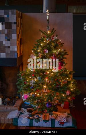 Ein dekorierter Weihnachtsbaum, beleuchtet von warmen Lichtern, steht drinnen, umgeben von Geschenken und einer gemütlichen Atmosphäre. Stockfoto