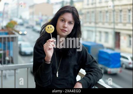 Eine Frau steht auf einem Balkon mit einem Lutscher mit lächelndem Gesicht, mit einem verschwommenen Hintergrund der Stadtstraße. Stockfoto