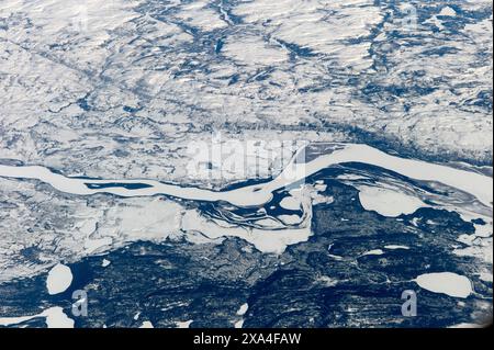 Ein Blick aus der Vogelperspektive auf eine schneebedeckte Landschaft mit einem sich windenden Fluss, der durch das eisige Gelände schneidet. Stockfoto