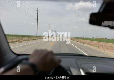 Ein Blick aus der Perspektive des Fahrers in ein Auto, das eine gerade Straße entlang fährt, gesäumt von Versorgungsmasten unter einem bewölkten Himmel. Stockfoto