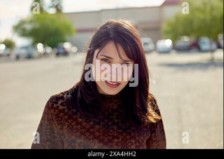 Eine lächelnde Frau mit dunklem Haar, die ein Spitzentop trägt, steht draußen an einem sonnigen Tag, mit Sonnenlicht, das ihr Haar hervorhebt. Stockfoto