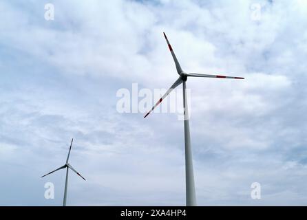 Zwei Windturbinen stehen hoch vor einem bewölkten Himmel, ihre Rotorblätter sind in unterschiedlichen Richtungen positioniert. Stockfoto