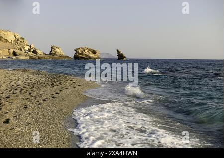 Ruhiger Strand mit sanften Wellen, die sich auf die Sandküste stürzen, mit zerklüfteten Klippen im Hintergrund unter klarem Himmel. Stockfoto