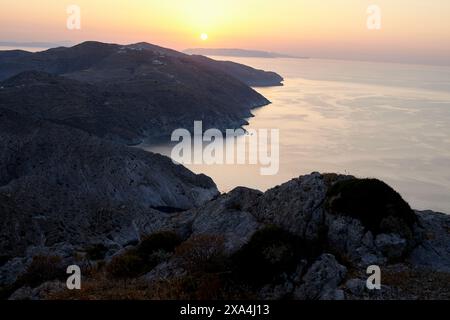 Ein ruhiger Sonnenuntergang über einer zerklüfteten Küste, während die Sonne ein warmes Licht über das Meer und felsiges Gelände wirft. Stockfoto