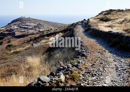 Ein Steinwanderweg führt durch eine trockene, grasbewachsene Landschaft zu einem weit entfernten Aussichtspunkt mit einem klaren blauen Himmel darüber. Stockfoto