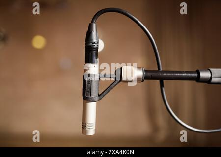 Nahaufnahme eines Mikrofons, das an ein Kabel mit verschwommenem Hintergrund angeschlossen ist und auf eine Musikaufnahme oder eine Aufführungsumgebung hinweist. Stockfoto