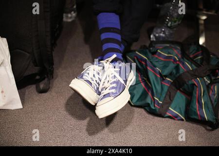 Eine Nahaufnahme der Füße einer Person mit blauen Socken und weißen Sneakers mit blauen Schnürsenkeln sowie einer grün gestreiften Sporttasche auf einem Teppichboden. Stockfoto