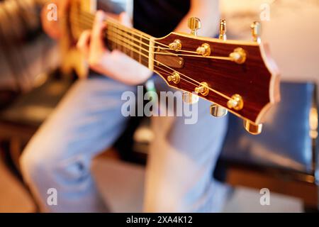 Eine Nahaufnahme eines Gitarrenkopfes, der gespielt wird, mit Fokus auf die Stimmstifte und verschwommene Hände und Saiten im Hintergrund. Stockfoto