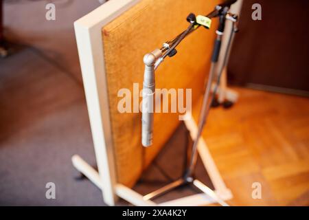 Nahaufnahme eines silbernen Mikrofons vor einem beigefarbenen Lautsprecherschrank auf Holzboden, mit selektivem Fokus und unscharfem Hintergrund. Stockfoto