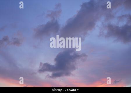 Das Bild zeigt einen ruhigen Himmel in der Dämmerung mit sanften Rosa- und Violetttönen, die von dunklen, schimmernden Wolken akzentuiert werden. Stockfoto