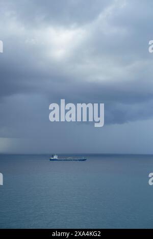 Ein einsames Schiff segelt auf einem riesigen Ozean unter einem dramatischen, stürmischen Himmel mit dunklen, bewölkten Wolken. Stockfoto