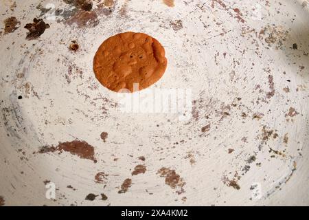 Ein einzelner, frisch gebackener Schokoladen-Chip-Keks befindet sich in der Mitte eines gut gebrauchten, gereiften Backblatts mit Keksrückständen um ihn herum. Stockfoto