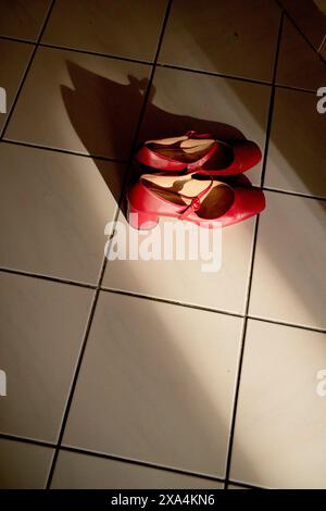 Ein Paar roter High-Heels-Schuhe auf weißem Fliesenboden wirft einen langen Schatten unter direkter Sonneneinstrahlung. Stockfoto