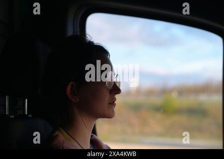 Eine Frau blickt während einer Fahrt aus einem Fahrzeugfenster, ihr Profil ist an der vorbeifahrenden Landschaft angelehnt. Stockfoto