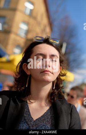 Eine junge Frau mit geschlossenen Augen steht draußen, ihr Gesicht ist teilweise von Sonnenlicht beleuchtet, mit Sonnenbrille auf dem Kopf. Stockfoto