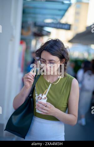 Eine Frau steht auf einer belebten Straße und genießt eine Tasse Eis. Stockfoto