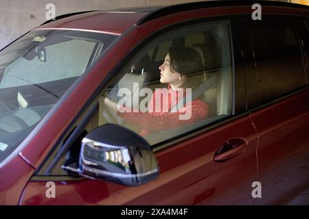 Eine fokussierte Person fährt ein rotes Auto durch eine Parkgarage. Stockfoto