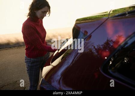 Eine Person öffnet während eines sonnigen Abends eine Autotür und strahlt ein warmes Licht auf die Szene aus. Stockfoto