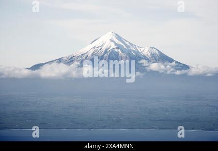 Der schneebedeckte Berggipfel erhebt sich über den Wolken, mit einem klaren Blick auf den Gipfel und einem Hauch der umliegenden Landschaft darunter, Mt. Taranaki, Neuseeland Stockfoto