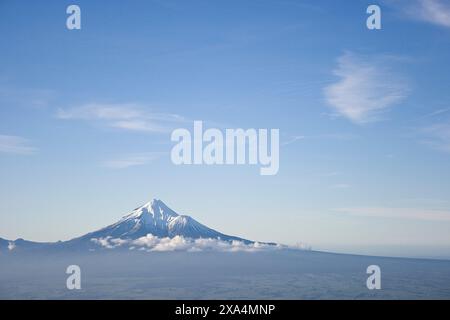 Ein schneebedeckter Vulkan erhebt sich majestätisch über einem Wolkenmeer unter einem klaren blauen Himmel, Mt. Taranaki, Neuseeland Stockfoto