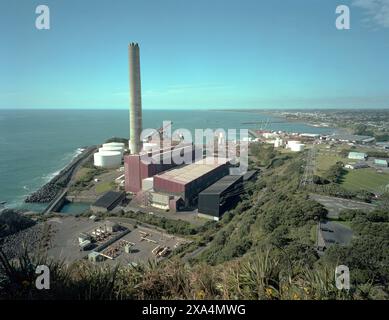 Ein Industriekomplex mit großen Lagertanks und einem hohen Schornsteinstapel befindet sich entlang einer Küste in New Plymouth, Neuseeland Stockfoto