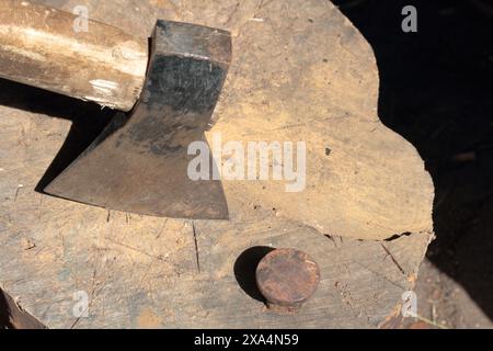 Die Axt ist in ein Holzdeck gehämmert. Als Nächstes ist ein Hammerbock zum Nieten einer Sense. Stockfoto