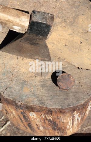 Die Axt ist in ein Holzdeck gehämmert. Als Nächstes ist ein Hammerbock zum Nieten einer Sense. Stockfoto