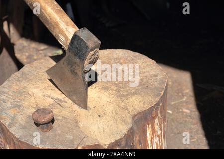 Die Axt ist in ein Holzdeck gehämmert. Als Nächstes ist ein Hammerbock zum Nieten einer Sense. Stockfoto