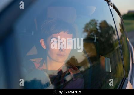 Eine junge Frau blickt in der Dämmerung durch ein Autofenster, mit Reflexionen auf dem Glas. Stockfoto