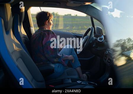 Eine junge Frau wird während eines frühen Abends beim Autofahren gesehen, während die goldene Sonne ihr Profil sanft beleuchtet. Stockfoto