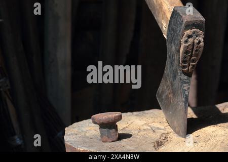 Die Axt ist in ein Holzdeck gehämmert. Als Nächstes ist ein Hammerbock zum Nieten einer Sense. Stockfoto