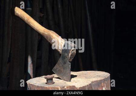 Die Axt ist in ein Holzdeck gehämmert. Als Nächstes ist ein Hammerbock zum Nieten einer Sense. Stockfoto