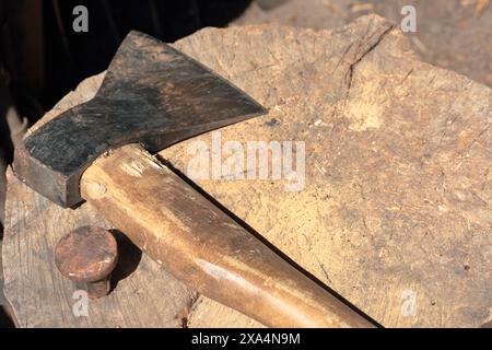 Die Axt liegt auf einem Holzdeck. Als Nächstes ist ein Hammerbock zum Nieten einer Sense. Stockfoto