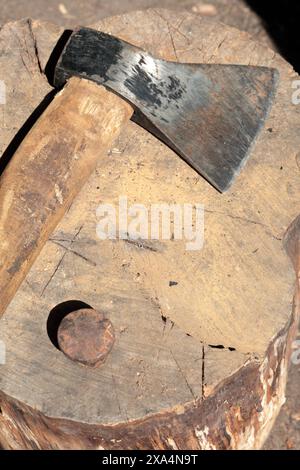 Die Axt liegt auf einem Holzdeck. Als Nächstes ist ein Hammerbock zum Nieten einer Sense. Stockfoto