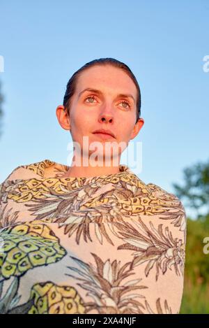 Eine Frau, die in eine gemusterte Decke gehüllt ist, blickt in die Ferne vor einem ruhigen Himmel in der Abenddämmerung. Stockfoto