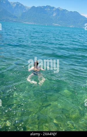 Ein Schwimmer genießt das klare türkisfarbene Wasser eines ruhigen Sees mit Blick auf die Berge im Hintergrund. Stockfoto