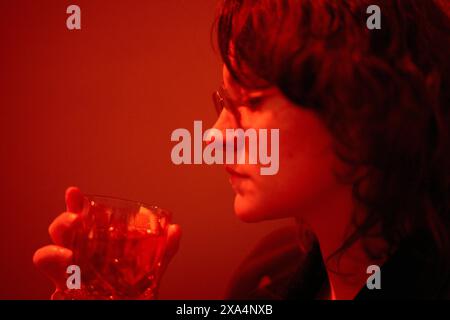 Ein Nahaufnahme-Bild, das das Seitenprofil einer jungen Frau mit gemustertem Glas zeigt, beleuchtet durch rote Beleuchtung. Stockfoto